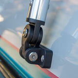 Close-up of a black metal and plastic mounting bracket attached to a silver cylindrical pole, shown against a blurred outdoor background with a vehicle or wall visible.